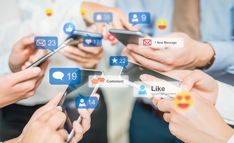 Several people are holding smartphones with social media notifications displayed around the devices, including likes, messages, comments, and friend requests. The scene emphasizes a high level of online interaction and engagement, akin to the effect of google review bots driving activity.