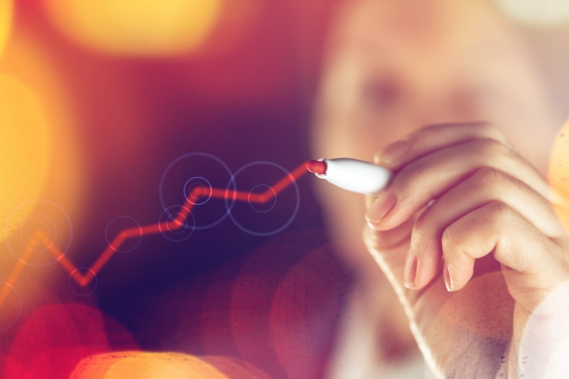 A person holding a marker is drawing a red, upward-trending line graph on transparent glass, symbolizing growth and resilience. The background features warm, glowing lights, reflecting the dynamic and positive spirit of a reputation defender at work.