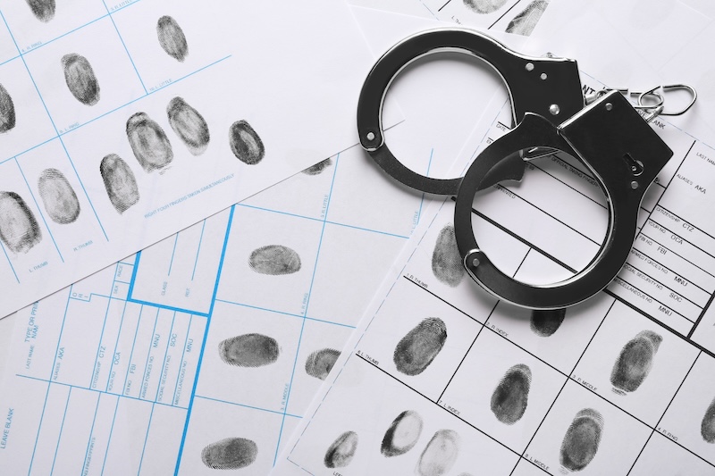 A crime scene unfolds with fingerprint sheets and a pair of handcuffs placed meticulously, evoking a scene of forensic analysis. One can't help but wonder how to get their mugshot off Google amidst such intriguing drama.