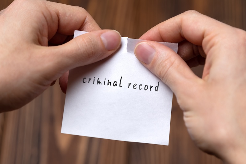 Hands tearing a piece of paper with the words "criminal record" printed on it, over a wooden surface, symbolizes breaking free from past mistakes, much like trying to get your mugshot off Google.