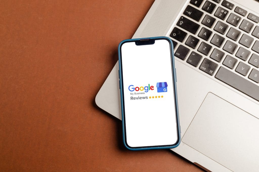 A phone with the google logo on it sits next to a laptop.