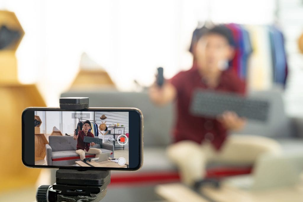 A man is using a smartphone to take a video of a woman in a living room.