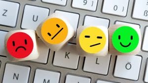 Wooden blocks with emoticons displaying various emotions: sad (red), neutral (orange), unsure (yellow), and happy (green), are placed on a computer keyboard.