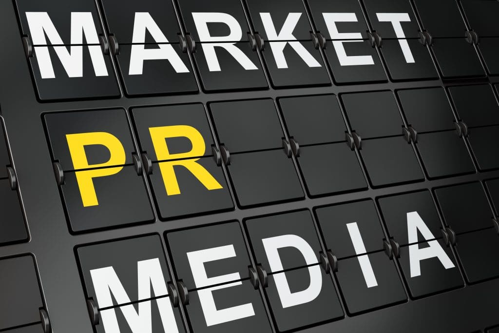 A mechanical flipboard-style display with the words "MARKET," "PR," and "MEDIA." The letters are in white except for "PR," which is in yellow. The background is a grid of black panels with hinge details.