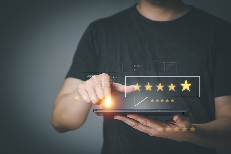 A person in a dark shirt is holding a tablet, interacting with a digital five-star rating system. Floating graphics of stars and rating icons are visible above the tablet.